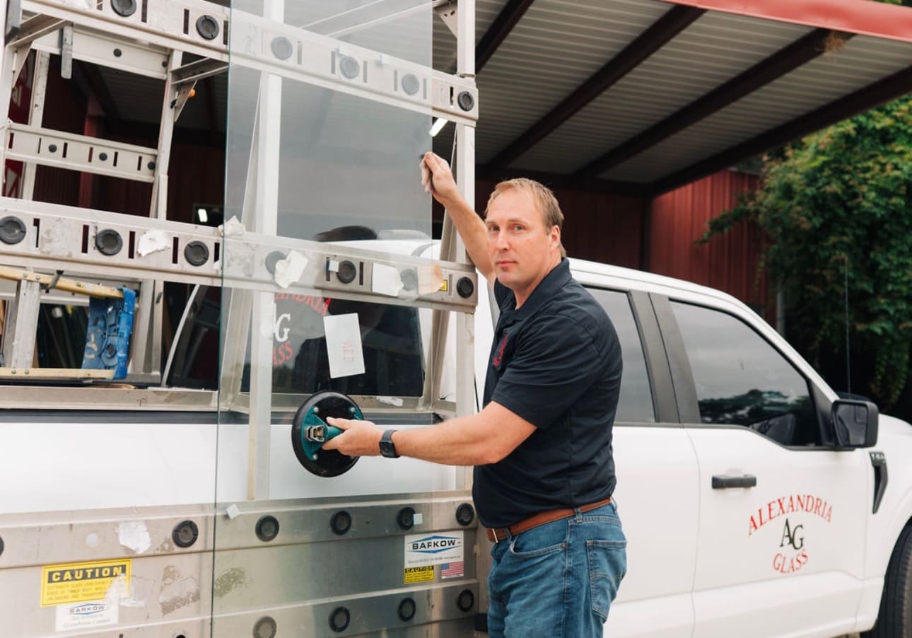 An Alexandria Glass installer loading a glass pane onto a service truck with a suction cup