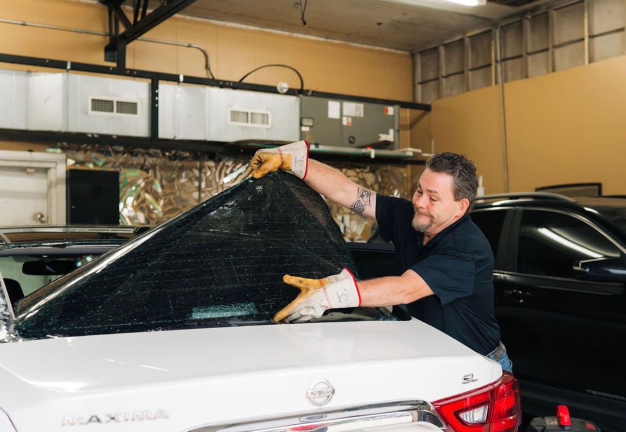 Technician removing a windshield from a Nissan in the shop bay